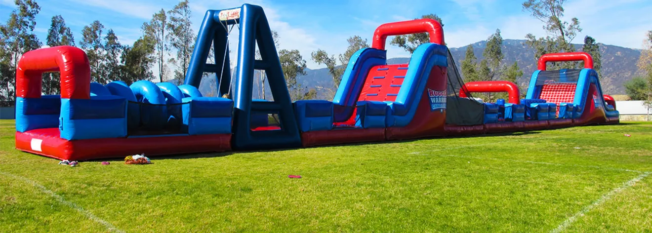 The Rugged Warrior Challenge set up end to end on a grass field: red and blue inflatable obstacle sections with arches, tunnels, climbing walls and slides